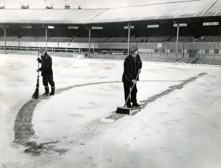 Two men sweeping snow at Dens Park. 
