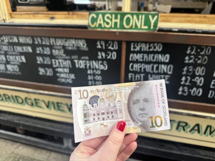 A £10 note held in front of a sign that reads "cash only" at The Auld Tram in Dundee. 