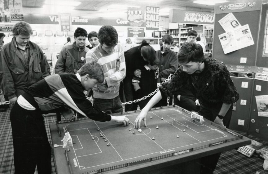 two boys play Subbutteo while others look on