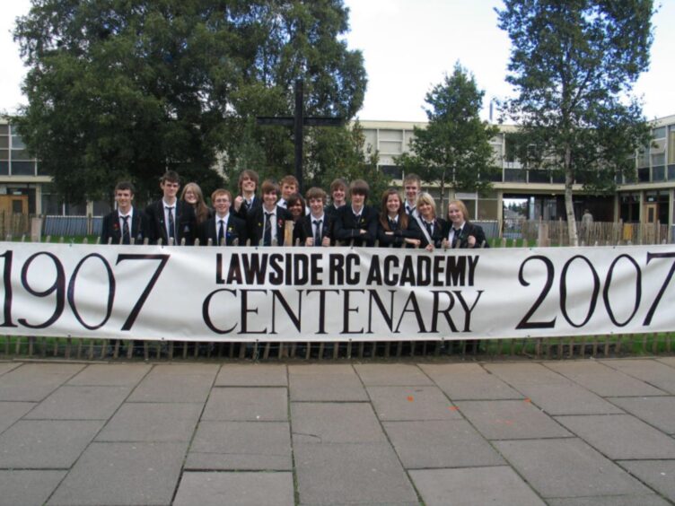 Pupils in a courtyard line up behind the school's centenary banner