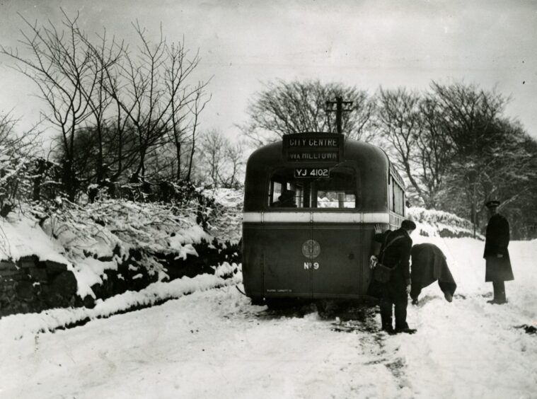 people stand beside a bus stuck in the snow