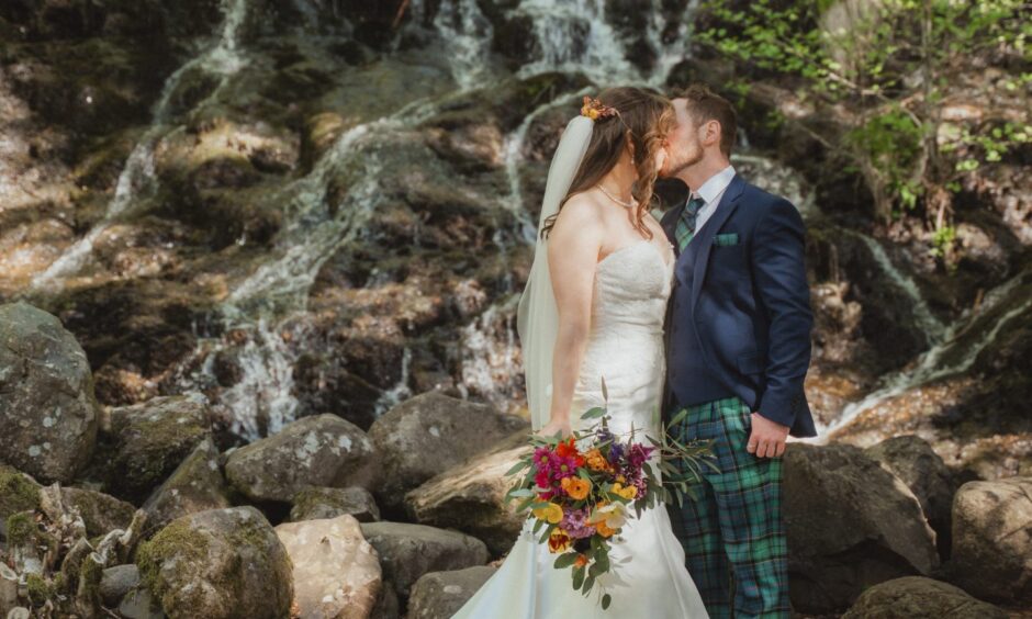 Couple kissing by a waterfall on their wedding day.
