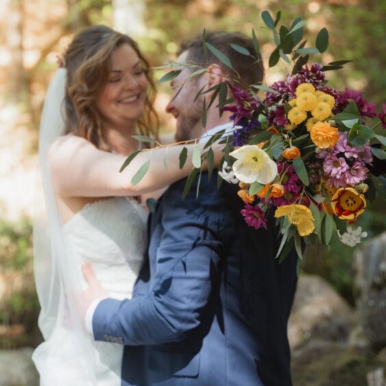 Just married, couple smiling and embracing, wedding flowers, woodland background.