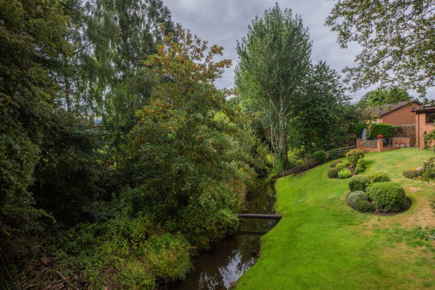 Burn in Bridge of Earn with neat garden on one side and overgrown trees and weeds on the other