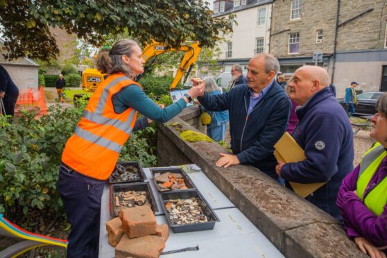 Woman in high vis tunic leaning over wall showing objects to members of public
