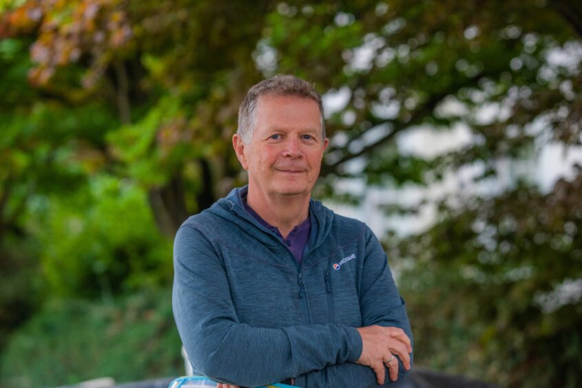 Richard Oram, arms folded, in front of tree
