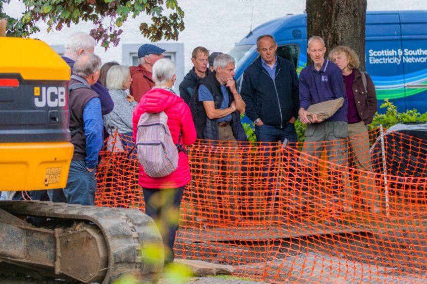 Group of people around hole in ground protected by fencing