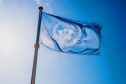 UN flag flies against a blue sky.