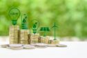Several stacks of coins, topped by symbolic green emblems including a battery, a wind turbine and a solar panel.