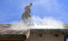 Worker power washes a house roof