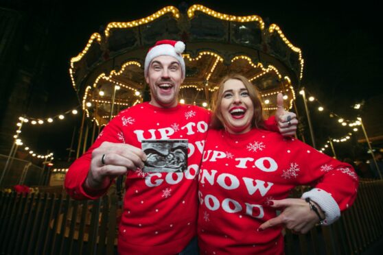 Drew Millard, 26,  and Ella Dean, 26, enjoy the Christmas Fair in Princes Street, Edinburgh, but the couple, from Yorkshire, have a special reason to celebrate as Drew holds up a baby scan after revealing to their friends and family that Ella is three months pregnant.