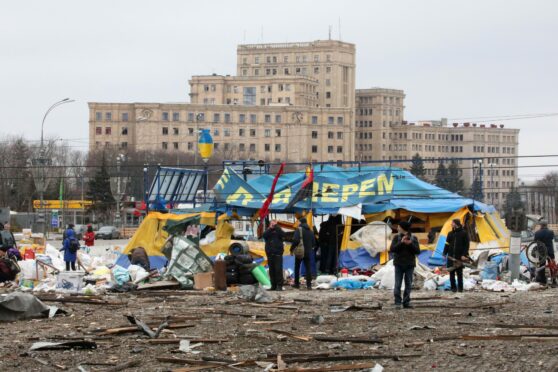 People stay by the All for Victory Tent of volunteers after a missile launched by Russian invaders hit outside the Kharkiv Regional State Administration building in Svobody (Freedom) Square.