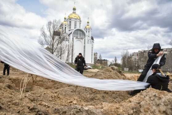 Police officers cover a mass grave containing 410 bodies of civilians in Bucha, Kyiv, last week as war crime prosecutors consider an arrest warrant against Vladimir Putin and his henchmen