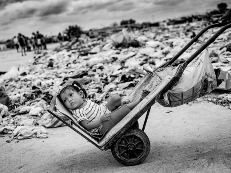 The Children of the Financial Collapse in Venezuela: A young girl being transported home by her dad along the garbage site, on the abandoned airstrip outside Maicao in Colombia.