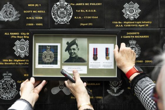 Relatives of Private James McPhilemy hold up his photo and medals at the plaque at Glasgow Central Station