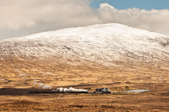 A steam train arrives into Corrour Station, with Beinn na Lap in the background