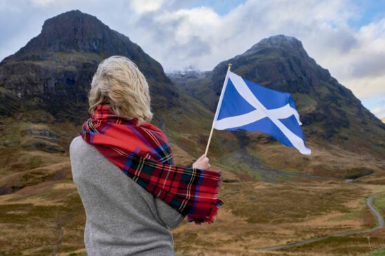 Women with Scotland flag admiring the Scottish panorama (image to correlate article about coach tour in Scotland)