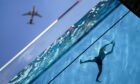 A plane flies overhead as man swims in the Sky Pool suspended 35 metres above the ground as temperatures soared in London last week