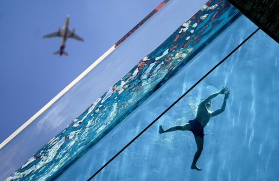 A plane flies overhead as man swims in the Sky Pool suspended 35 metres above the ground as temperatures soared in London last week