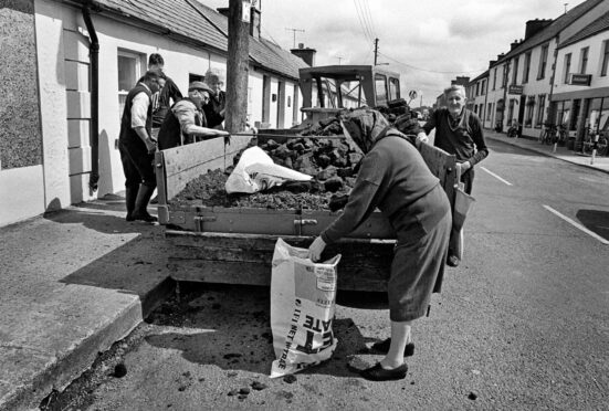 A woman collects a bag of peat for her kitchen fire from a street delivery man in Ireland in 1990