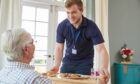 Male care worker serving older man meal in a care home