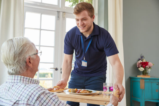 Male care worker serving older man meal in a care home