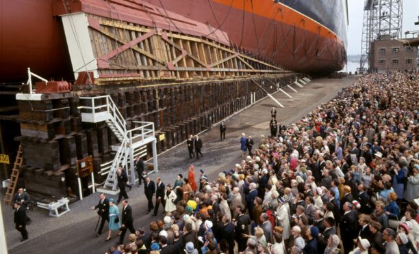 The Queen, in blue coat, passes the QE2 and huge crowds as she launches the liner in 1967