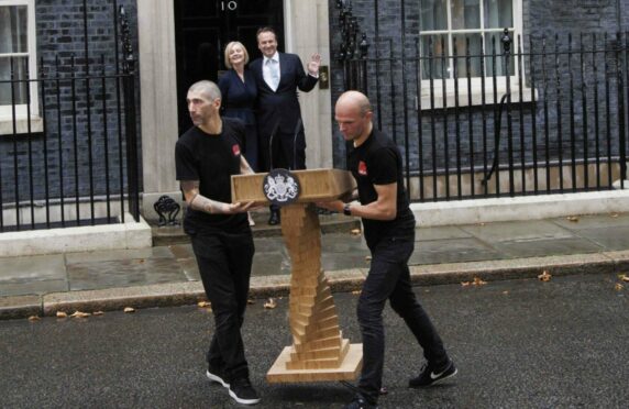 As workmen clear away the lectern where she made her first speech as PM, Liz Truss and husband, Hugh O’Leary, wave from the steps of 10 Downing Street on Tuesday