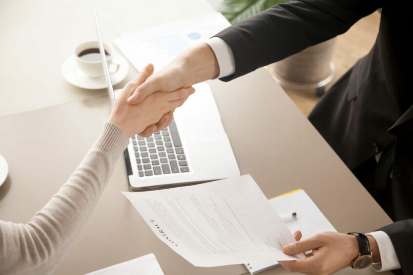 Man and woman shaking hands over laptop and coffee.