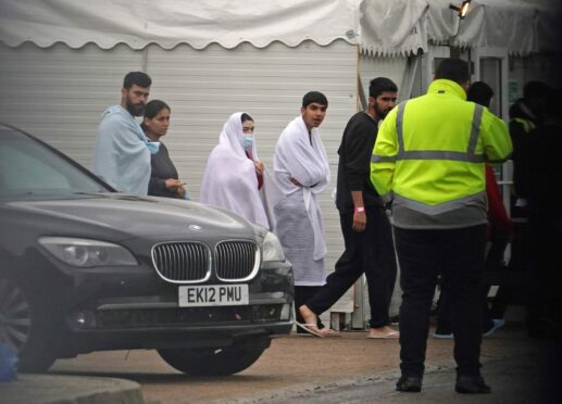 People thought to be migrants pass the car of Home Secretary Suella Braverman  (left) during her visit to the Manston immigration short-term holding facility.