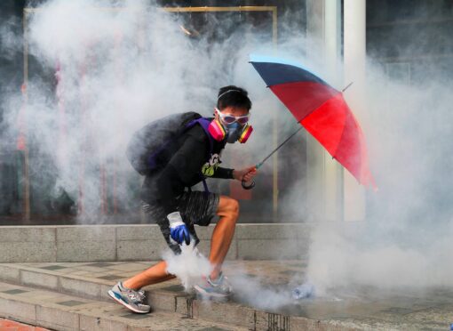 A protester holds an umbrella as he lifts a tear-gas canister fired by police in Hong Kong
