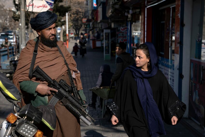 A Taliban fighter stands guard in Kabul on Monday as a woman walks past