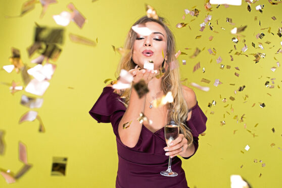 Beautiful young woman with champagne amuse and dancing. Girl blows off sequins. Happy New Year; Shutterstock ID 723320878; purchase_order: Sunday Post; job: Sunday Post