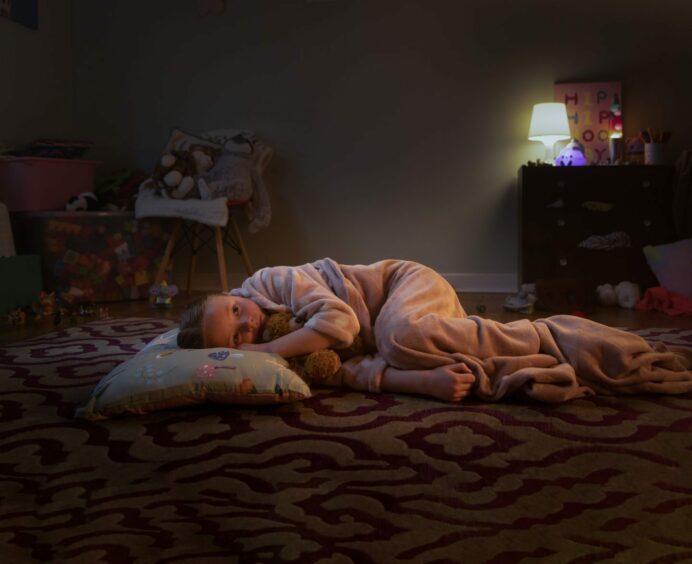 A child lying in a dark room with no blanket.