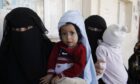 Women, holding their children suffering malnutrition, wait to get monthly shares of food aid in Sana’a in war-torn Yemen