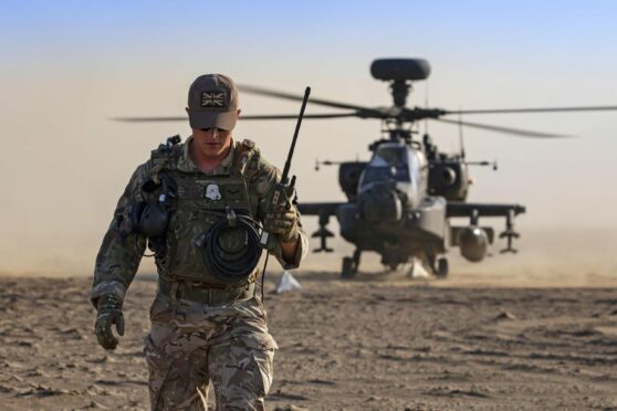 Service personnel monitor Apache helicopter conducting dust landing training at RAF base in Oman