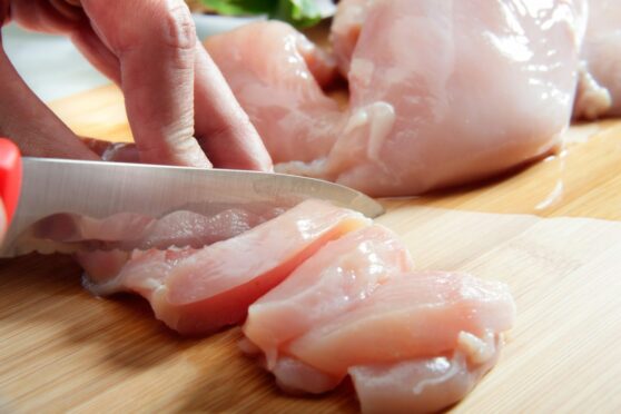 Hands cutting raw chicken.