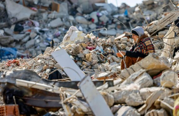 A woman sits amid rubble in Samandag, Turkey, after the earthquake