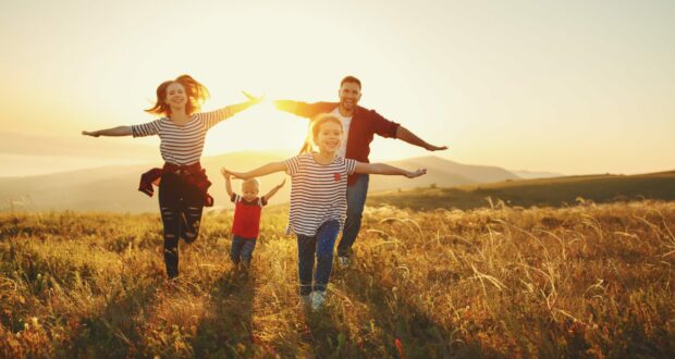 Happy family walking through a field at sunset.