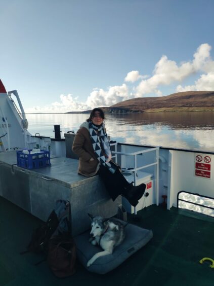 Writer Cal Flyn with husky Suka on a ferry in Orkney, with the hills of Hoy in the background