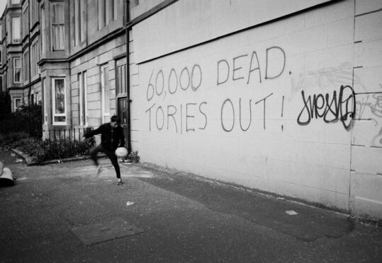 A boy plays in the streets of Govanhill, Glasgow, as graffiti charts the mounting death toll during the pandemic.