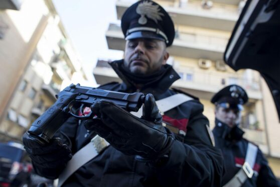 A police officer with a gun seized during searches in Ostia – mafia territory that is also a tourist haven