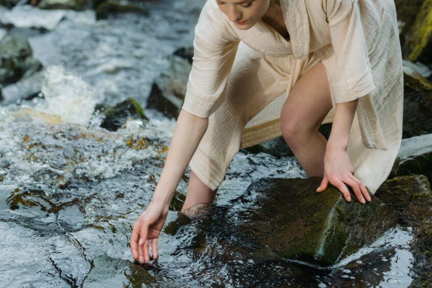 Woman touching water in stream.