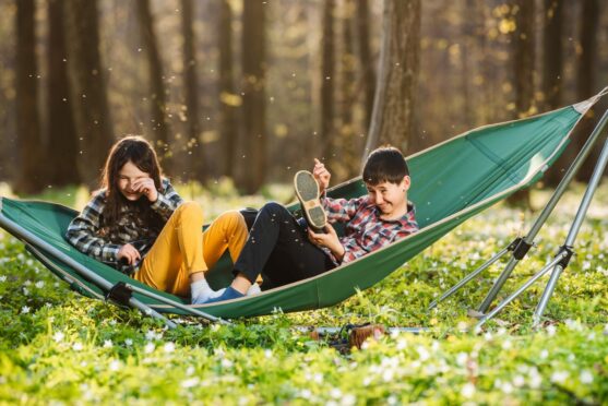 a girl and a boy on a hammock in a forest are swarmed by insects