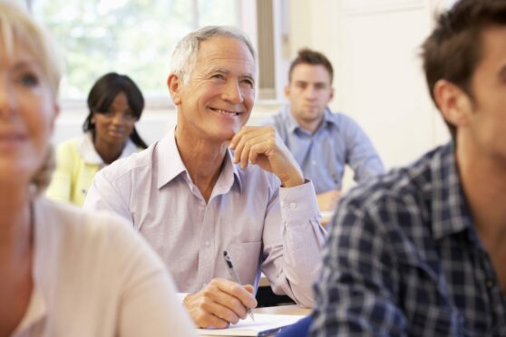 older man smiles as he sits in class with other students