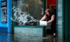 The owner of HQC Hairdressers in Glasgow, pours buckets of water out of her flooded salon.