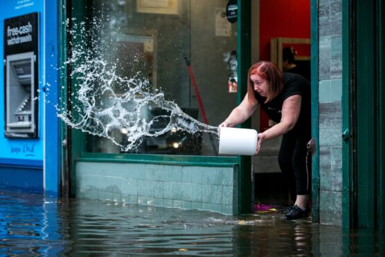 The owner of HQC Hairdressers in Glasgow, pours buckets of water out of her flooded salon.