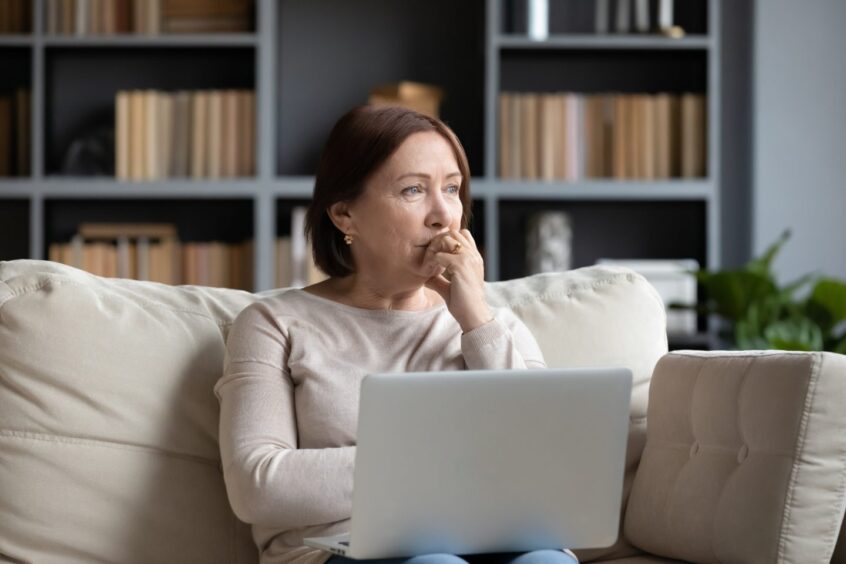 Woman mulling over a decision in front of a laptop.