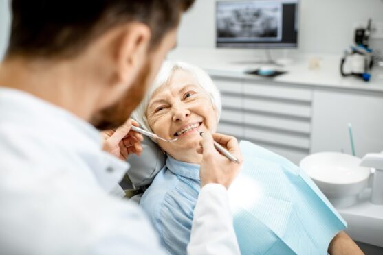 dentist examines teeth of smiling elderly woman who got implant-supported dentures