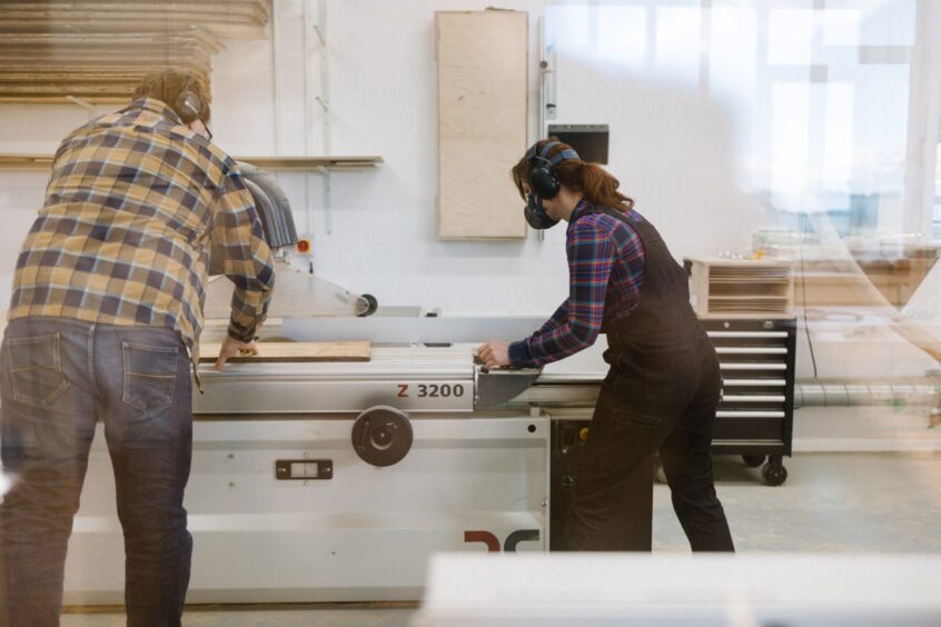 Adam and Vanessa in the workshop using a saw.